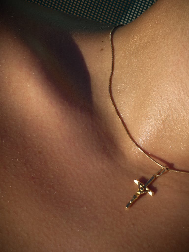 A close-up view of a gold cross necklace resting on bare skin in a faceless composition.