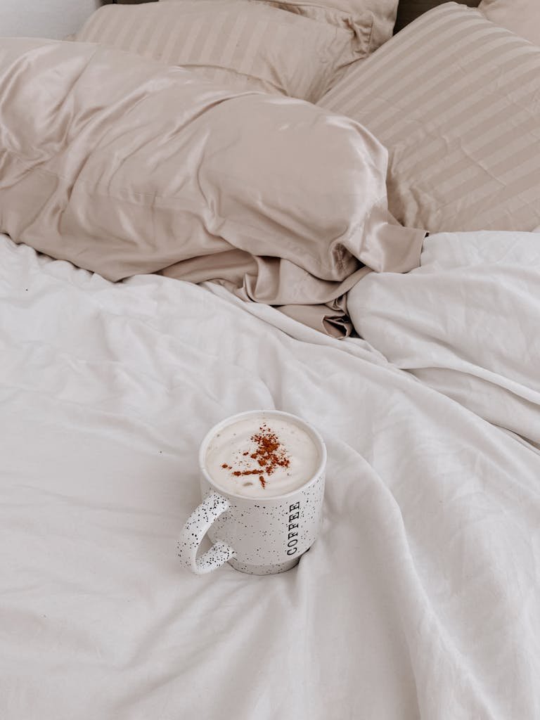 A cozy cup of coffee on a beige linen bed, perfect for a relaxed morning atmosphere.