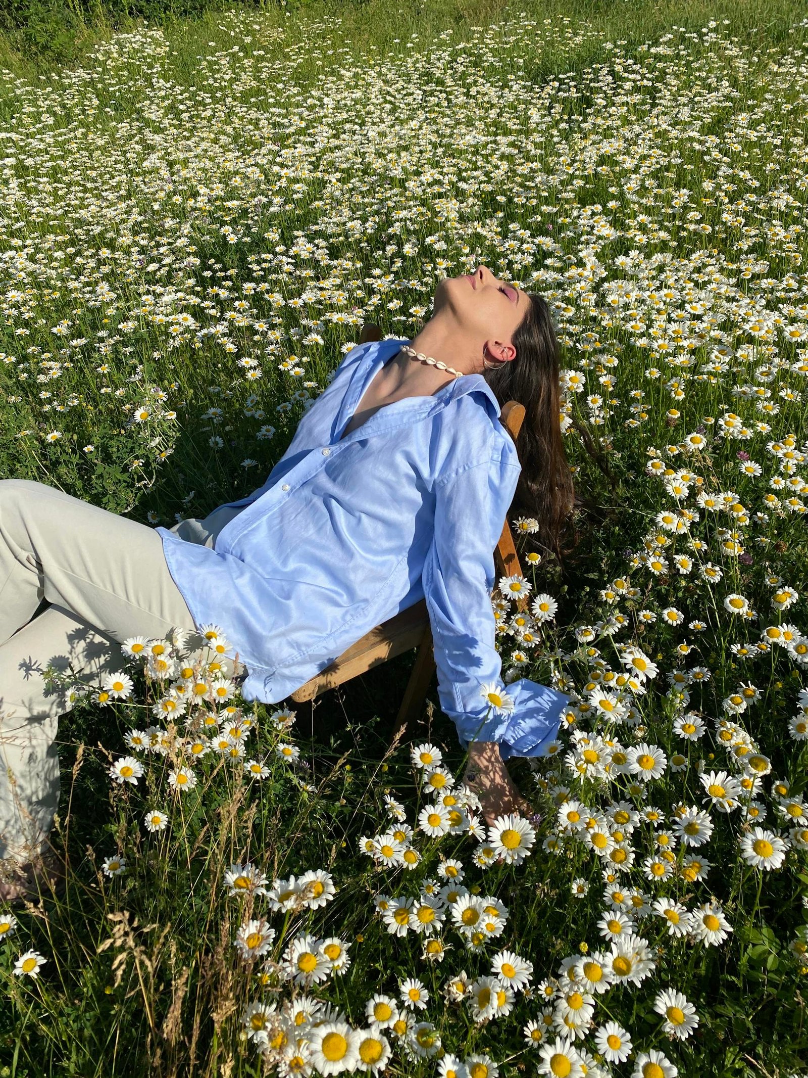 A woman in a blue shirt relaxing in a vibrant chamomile field on a sunny day.