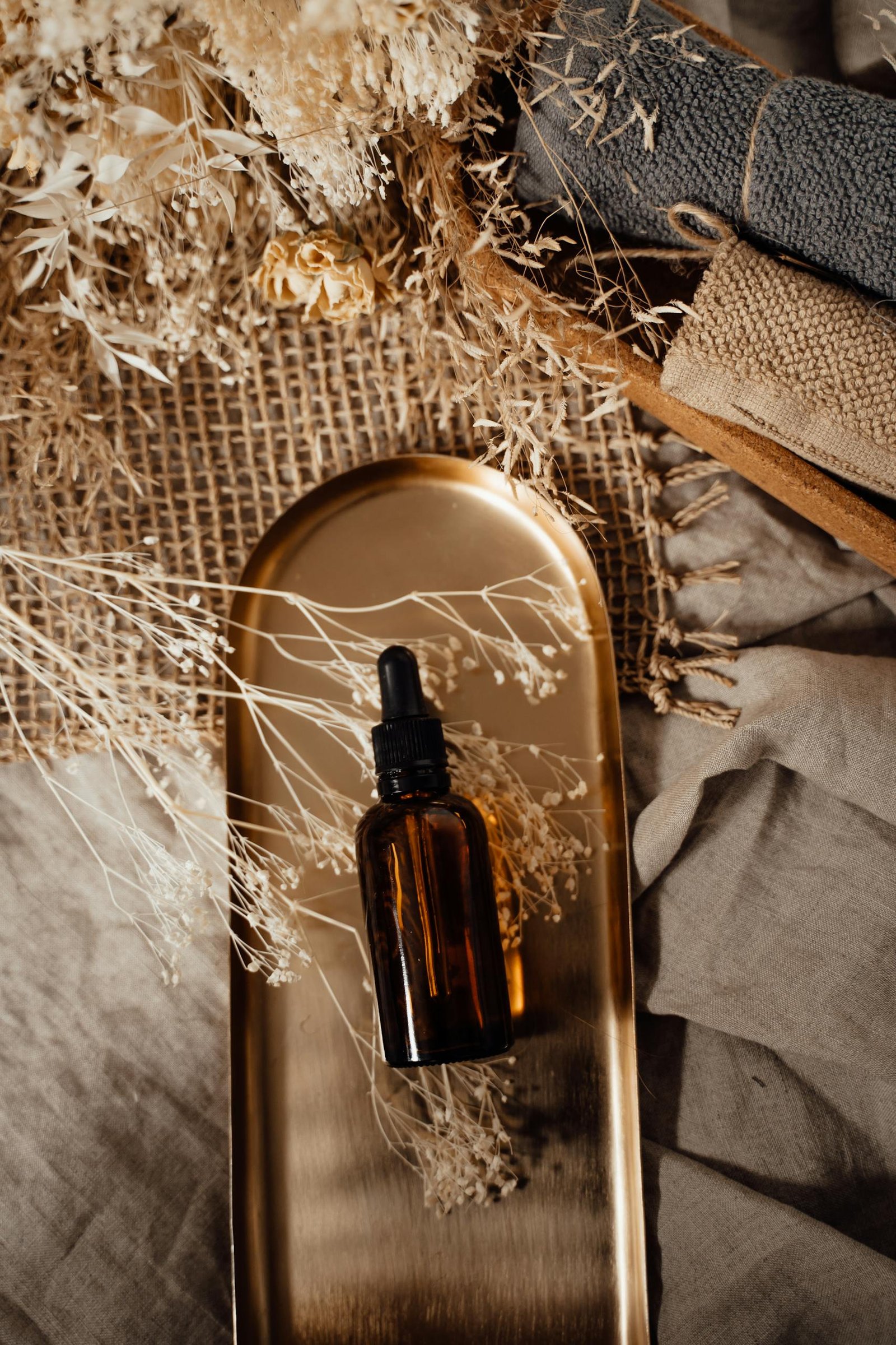 Amber dropper bottle placed on a gold tray among dried flowers, creating a warm and earthy still life composition.